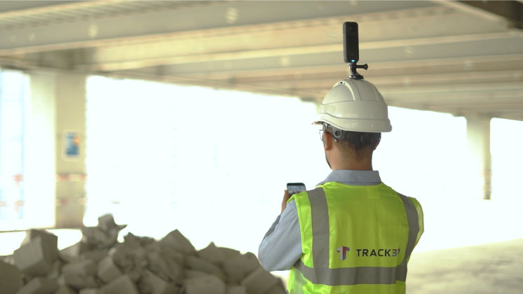 A construction engineer wearing an Insta360 X5 camera mounted on a hard hat while using a smartphone to review real-time site data and documented assets through the Track3D integration.